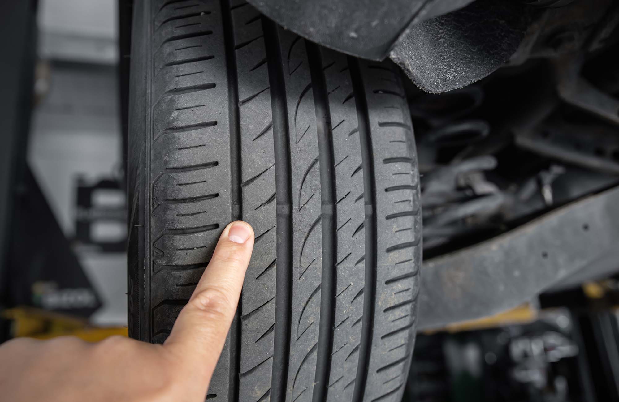 Mechanic pointing with hand at tyre wear indicator at car service center. Vehicle wheel protector control and inspection during maintenance. Tread wear check test inspection at automotive maintenance.